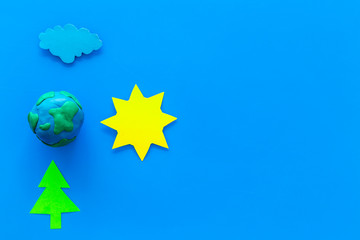 Environment protection concept. Plastiline symbol of planet Earth and sun, cloud, tree coutout on blue background top view copy space