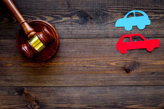 Car accident lawsuit concept. Two collided cars near judge gavel on dark wooden background top view copy space