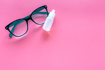 Eye drops in small bottle near glasses on pink background top view copy space