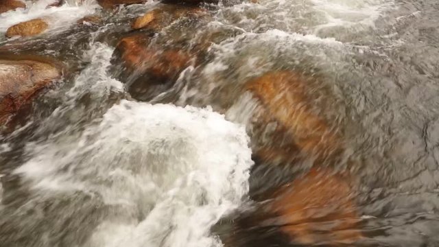 Rugged mountain river scenery panning panoramic with cascading mountain water running around large pebbles, boulders, high definition stock footage movie clip.