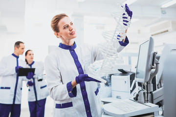 Gene evolution. Positive medical worker keeping smile on her face while looking at molecular chain