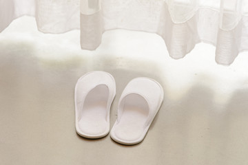 White slippers by white sheer curtains and soft sunlight, vacation concept