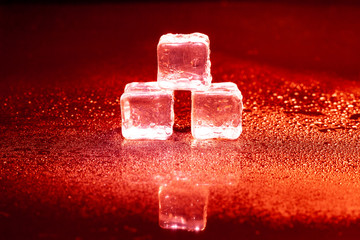 Red ice cubes reflection on black table.