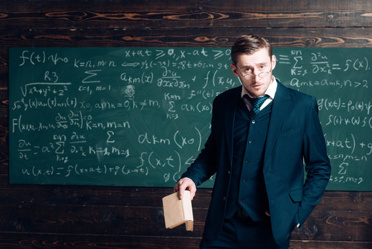 Exacting teacher. Teacher formal wear and glasses looks smart, chalkboard background. Man with high expectations looks unsatisfied with students knowledge. Professor exacting and strict holds book