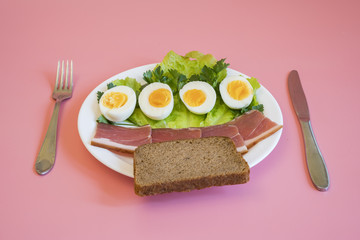 breakfast. Boiled eggs, bacon, greens bread in a white plate on pink background