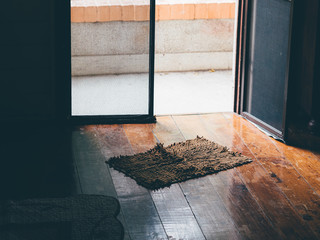 Vintage photo of soft doormat on old wooden floor of front door.