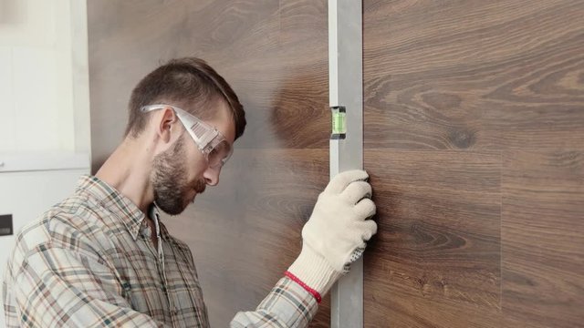 An adult engineer in uniform measures a brick wall with a level, an architect in a protective helmet checks the data of a building instrument