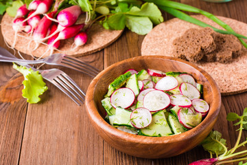 Lenten spring vegetable salad of cucumber, radish, greens and sunflower oil in a plate on a wooden table