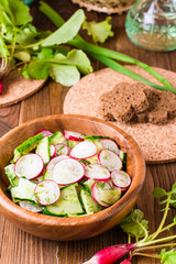 Lenten spring vegetable salad of cucumber, radish, greens and sunflower oil in a plate on a wooden table