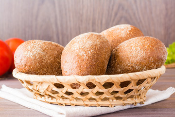 Fresh rye buns in a basket, salad and tomato on a wooden table