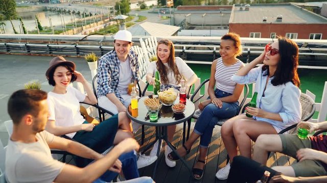 Happy friends are putting hands together then raising them celebrating success sitting at table on rooftop, laughing and talking. Friendship and party concept.