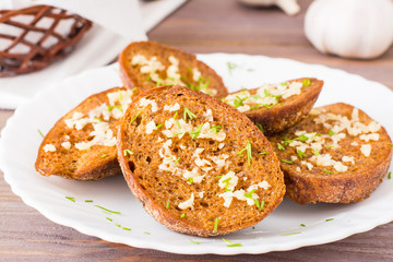 Close-up of fresh rye garlic croutons with dill on a plate on a wooden table