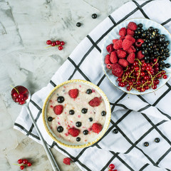 A bowl of oatmeal with berries on a checkered white napkin next to a plate of red and black currants and raspberries. Healthy Food Concept