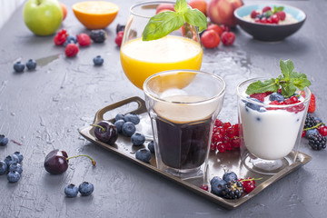 Delicious and healthy breakfast, gray background and napkin. Yogurt, muesli, granola, raspberry and blueberry berries, fresh orange juice and fragrant morning coffee. Copy space. Above.