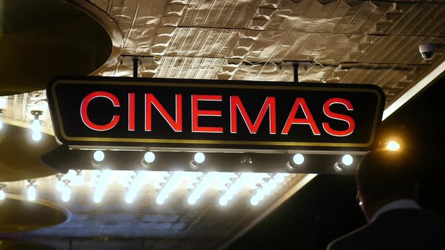 Cinema Sign at Street Entrance to Movie Theatre and Box Office with People Walking Past at Night