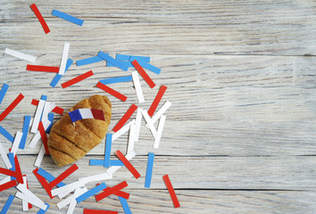 Paper confetti of national colors of France, white-blue-red on a white wooden background with flags and croissants, concept Bastille day, July 14 in France