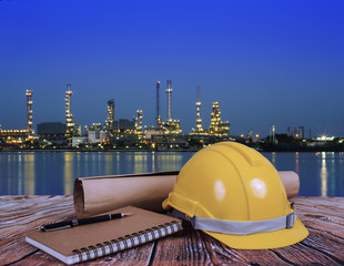Safety Helmets and Book on Table Over Blurred Oil refinery at night .