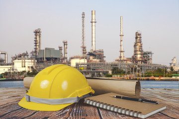 Safety Helmets and Book on Table Over Blurred Oil refinery background.