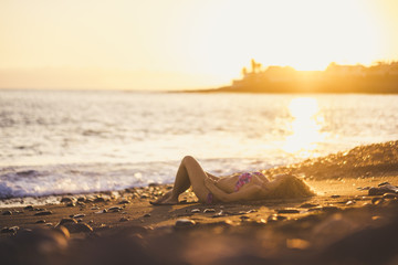 Fototapeta na wymiar relaxed young caucasian lady lay down on the shore near the ocean waves at the beach. summer sunset time for vacation and travel concept out of work and city lifestyle. golden colors and sunlight