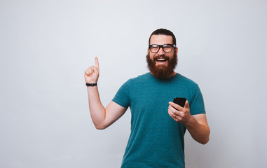 Naklejka premium Portrait of an excited young bearded man and mobile phone while pointing finger up