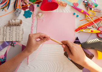Top view of table with elements for scrapbooking, tools for decoration and handmade albums and hands of master.