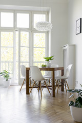 White chairs at table under lamp in bright dining room interior with balcony. Real photo