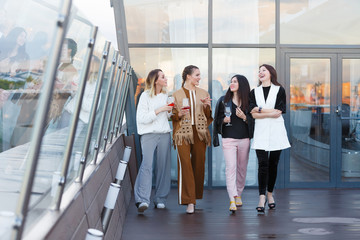 Four successful young female employees of large business companies celebrate a corporate party with a glass of wine in hands on an outdoor terrace