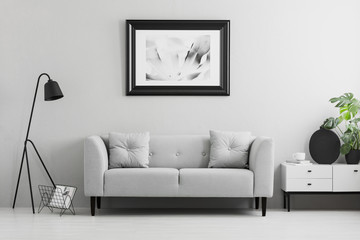 Framed photo on a wall above a fancy, gray sofa with cushions in a minimalist living room interior and place for a table. Real photo.