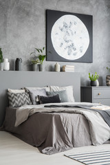 Vertical view of a modern bedroom interior in grey color with a big bed with pillows and bedding in the front and a moon painting on the wall. Real photo