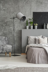 Grey bedroom interior with an elegant standing lamp with fabric shade between an armchair and a bed...