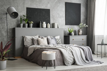 Stylish bedroom interior in grey with a big bed with bedsheets, pillows and blankets. A drawer...