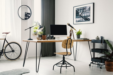 Wooden chair at desk with computer desktop in bright workspace interior with bike and poster. Real...