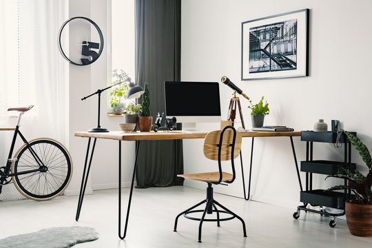 Wooden chair at desk with computer desktop in bright workspace interior with bike and poster. Real photo