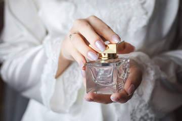 Close up shoot of a luxury perfume flacon being holded in manicured hands of elegant bride wearing...