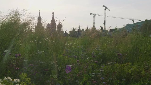 View of people sitting on grass of grassplot with Kremlin and building crane on background in evening