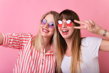 Two young girl friends standing together and having fun. Showing signs with their hands. Looking at camera and smiling. Inside