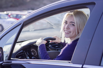 Fototapeta na wymiar Young woman driving a car in the city. Portrait of a beautiful woman in a car, looking out of the window and smiling
