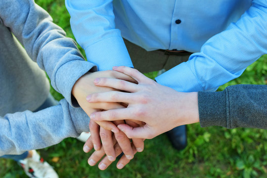 Stack of family people hands on green grass background outdoors. Family business and unity concept.