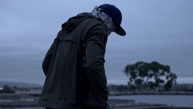 Rotating shot of a gang member with cap and mask on a rooftop with parallax effect.