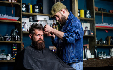 Hipster client getting haircut. Barber with hair clipper works on hairstyle for bearded man...