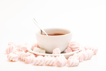 Tea cup with hot drink and marshmallows. Tea break concept. Process of drink brewing in mug. Mug filled with black brewed tea, spoon and heap of marshmallow on white background