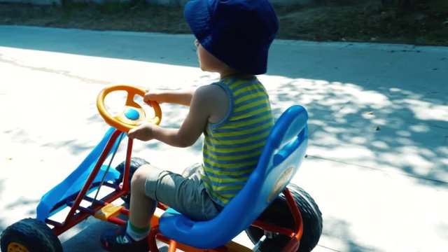 Little cute boy having fun driving a pedal car in the park. 4K