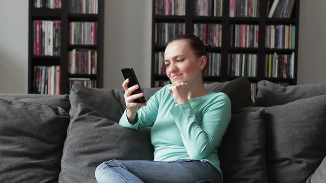 Woman at home messaging online with smartphone on grey couch