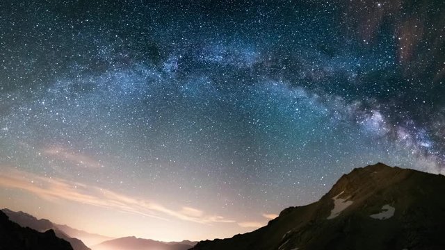 Milky Way arch and starry sky on the Alps. Panoramic view, astro photography, stargazing. Light pollution in the valley below.