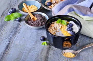 Yogurt with muesli, blueberries, poppy seeds, mint and crushed cornflakes served in black shiny bowl