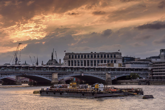 The river Thames, London, set against a dramatic red and orange sunset. There is a working barge in the foreground of the image