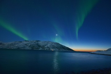 Fototapeta na wymiar The northern lights (Aurora Borealis) over Seljelvnes, Troms by the sea and the snowy mountains