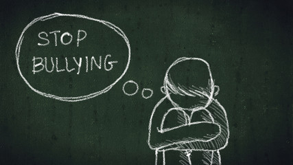sad young boy sitting on the floor with text stop bullying written with chalk on chalkboard. social problems of humanity - obrazy, fototapety, plakaty