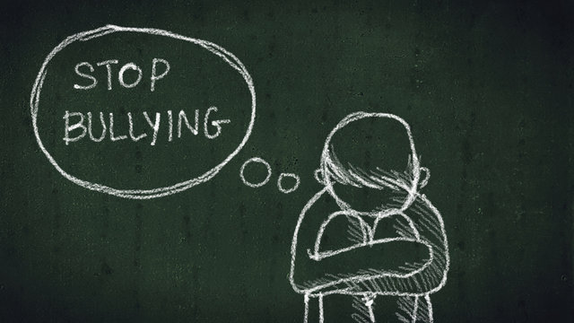 sad young boy sitting on the floor with text stop bullying written with chalk on chalkboard. social problems of humanity