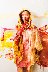 beautiful woman in raincoat painted with yellow and red paints showing silence gesture
